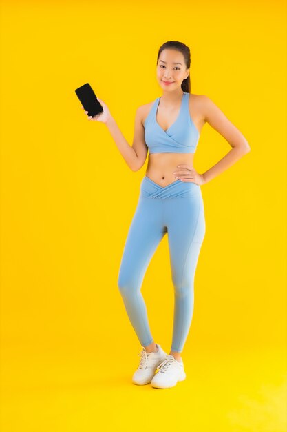 Женщина портрета красивая молодая азиатская с умным изолированным мобильным телефоном на желтом цвете