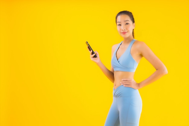 Женщина портрета красивая молодая азиатская с умным изолированным мобильным телефоном на желтом цвете