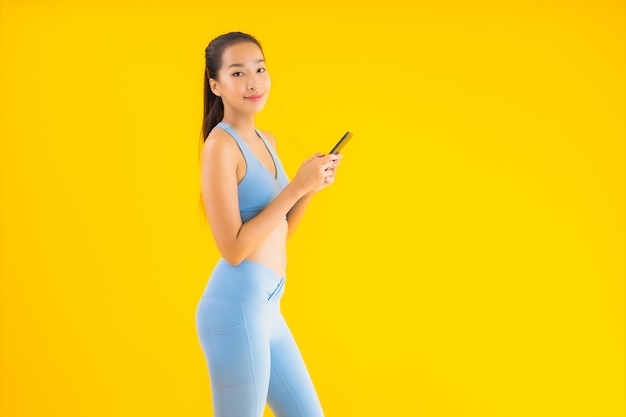 Bella giovane donna asiatica del ritratto con il telefono cellulare astuto su giallo isolato