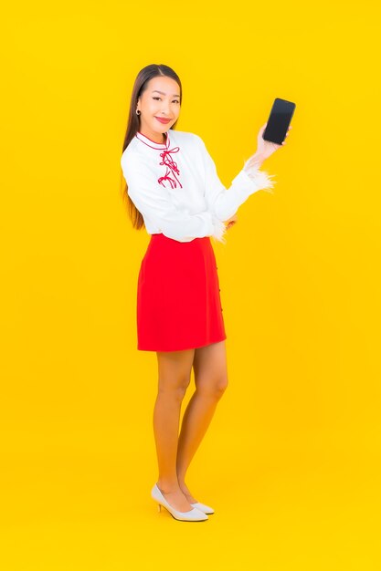 Женщина портрета красивая молодая азиатская с умным мобильным телефоном на желтом