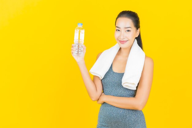 Portrait beautiful young asian woman with sportswear and bottle water on yellow wall