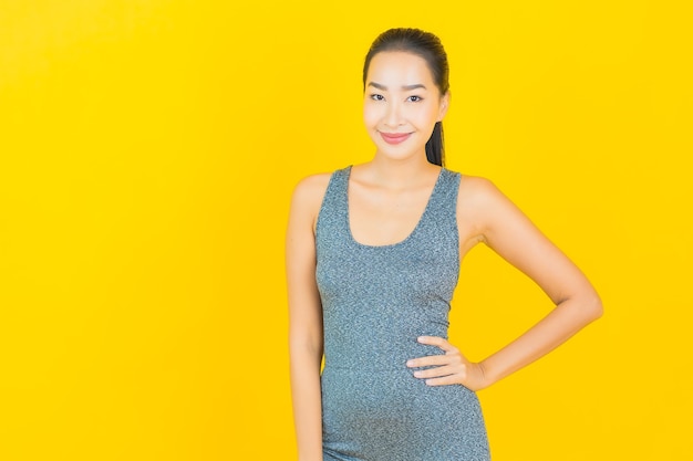 Женщина портрета красивая молодая азиатская с спортивной одеждой готова для тренировки на желтой стене