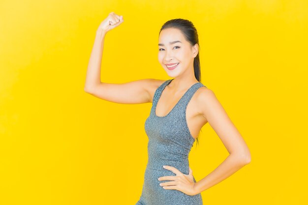 Женщина портрета красивая молодая азиатская с спортивной одеждой готова для тренировки на желтой стене