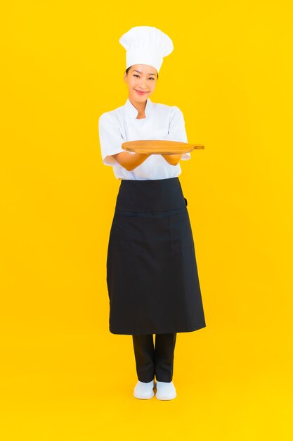 Portrait beautiful young asian woman with wooden cutting board on yellow isolated background