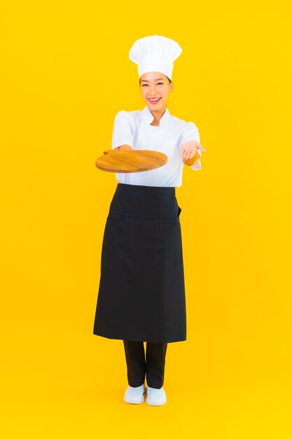 노란색 고립 된 배경에 나무 커팅 보드와 함께 초상화 아름 다운 젊은 아시아 여자