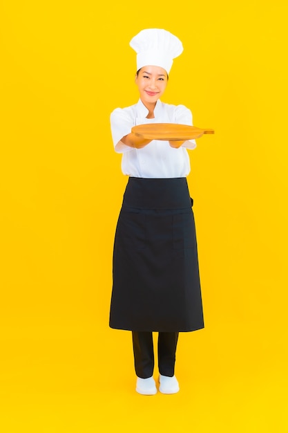 Portrait beautiful young asian woman with wooden cutting board on yellow isolated background