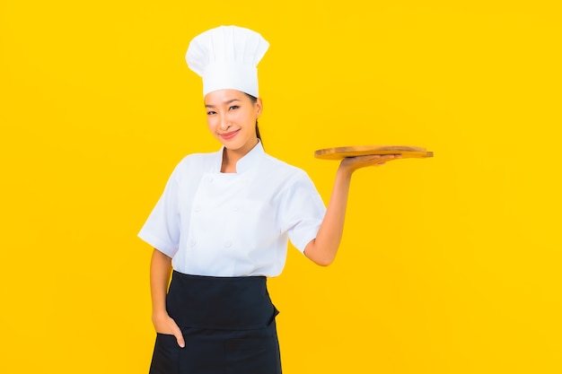 Portrait beautiful young asian woman with wooden cutting board on yellow isolated background