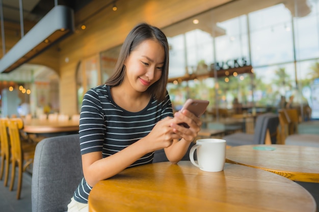 コーヒーショップカフェやレストランの携帯電話で美しい若いアジア女性の肖像画