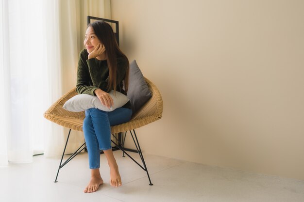 肖像画美しい若いアジア女性の幸せな笑顔はソファの椅子に座ってリラックスします。