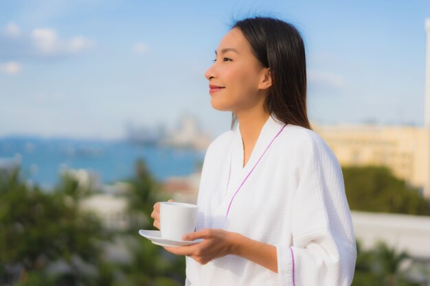 美しい若いアジア女性の肖像画は屋外の景色の周りに手でコーヒーカップを保持します。