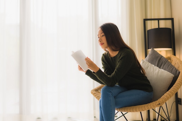 세로 아름다운 젊은 아시아 여성 책을 읽고 소파 의자에 앉아