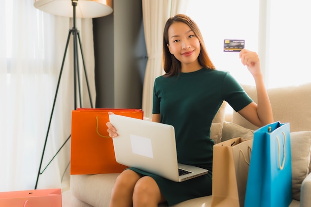 Женщины портрета красивые молодые азиатские используя компьтер-книжку компьютера с кредитной карточкой для онлайн покупок