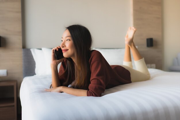 침대에 휴대 전화를 사용하여 세로 아름다운 젊은 아시아 여성