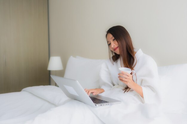침대에 커피 컵과 컴퓨터 노트북 세로 아름다운 젊은 아시아 여성