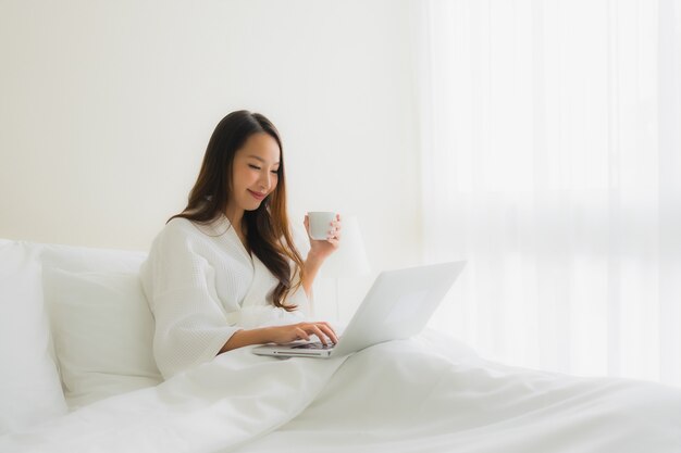침대에 커피 컵과 컴퓨터 노트북 초상화 아름 다운 젊은 아시아 여성