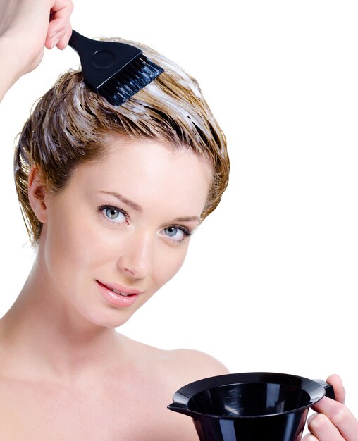 Portrait of beautiful young blond woman with bowl for hair-dye coloring her head isolated on white