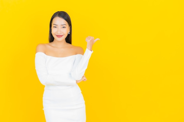 Portrait of beautiful young business asian woman smiling and pointing aside with white suit on yellow wall