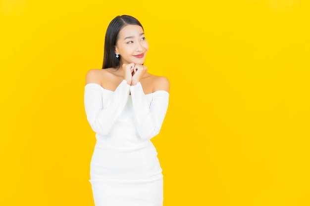 Портрет красивой молодой деловой азиатской женщины, улыбающейся с белым платьем на желтой стене
