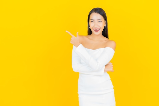 노란색 벽에 흰 드레스와 함께 웃 고 아름 다운 젊은 비즈니스 아시아 여자의 초상화