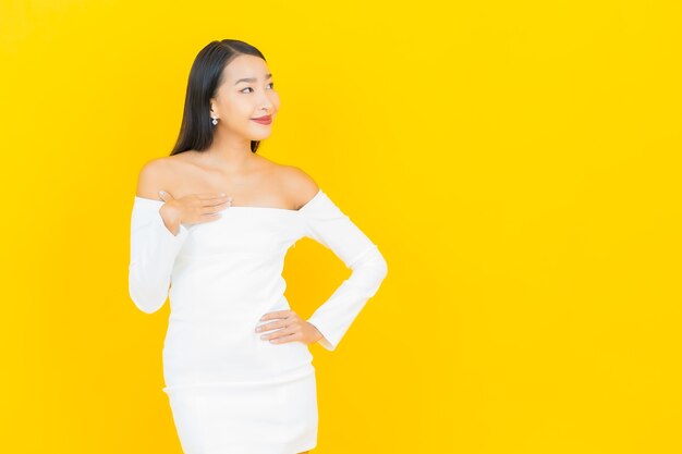 黄色の壁に白いドレスで笑って美しい若いビジネスアジアの女性の肖像画