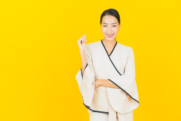 黄色の壁に白いスーツと笑顔の美しい若いビジネスアジア女性の肖像画