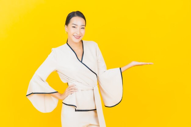 Portrait of beautiful young business asian woman smiling with white suit on yellow wall