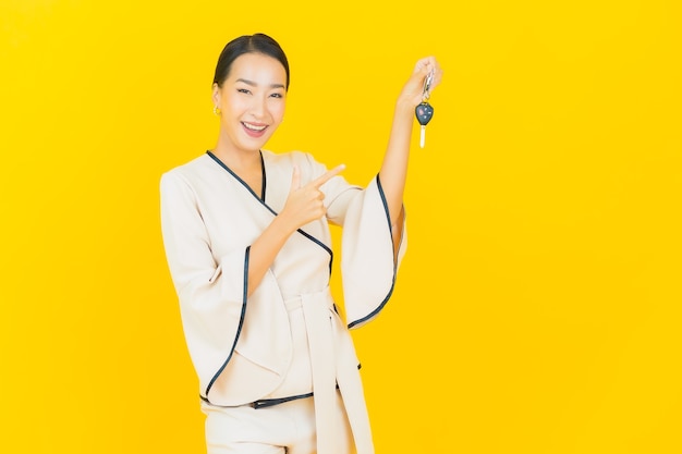 Portrait of beautiful young business asian woman with car key on yellow wall