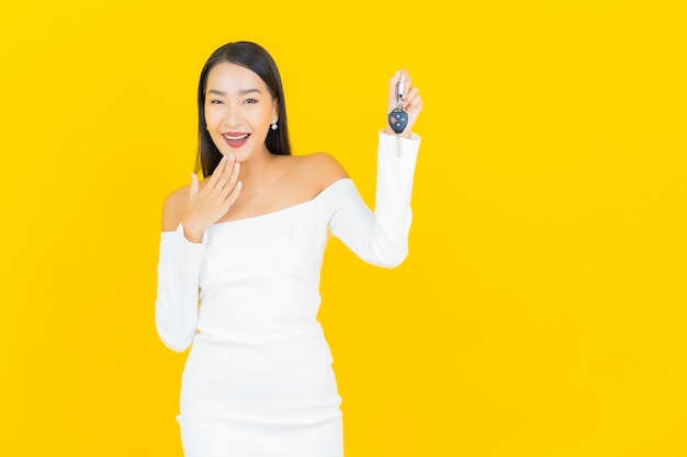 Portrait of beautiful young business asian woman with car key on yellow wall