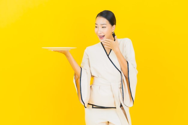 Portrait of beautiful young business asian woman with empty dish plate on yellow wall