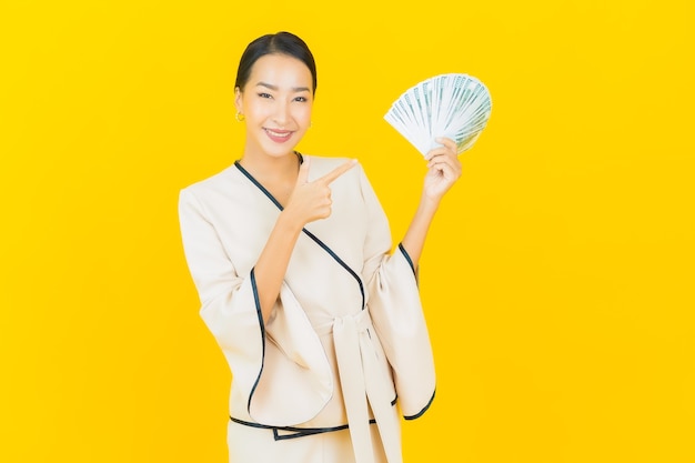 Portrait of beautiful young business asian woman with a lot of cash money and piggy bank on yellow wall