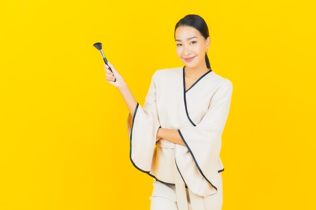 Portrait of beautiful young business asian woman with make up cosmetic brush on yellow wall