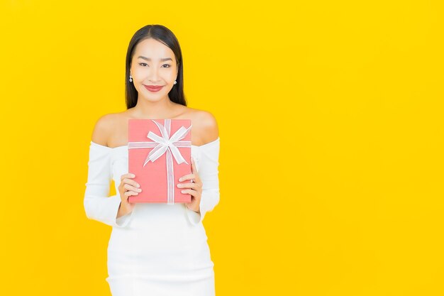 黄色の壁に赤いギフトボックスを持つ美しい若いビジネスアジアの女性の肖像画