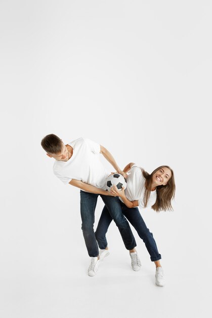 Portrait of beautiful young couple football or soccer fans on white studio background. Facial expression, human emotions, advertising, sport concept. Woman and man jumping, screaming, having fun.