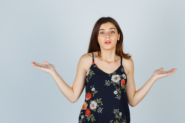 Portrait of beautiful young female showing helpless gesture in blouse