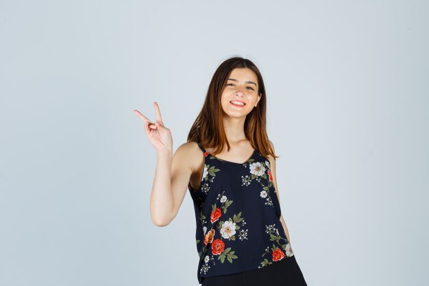 Portrait of beautiful young female showing victory gesture in blouse