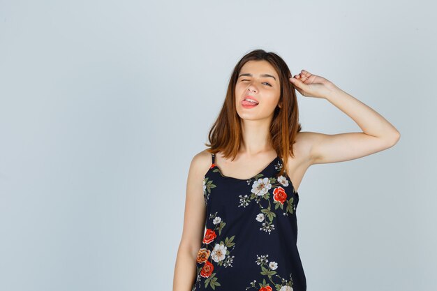 Portrait of beautiful young female touching hair while sticking out tongue