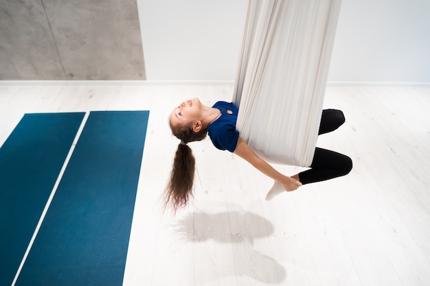 Free photo portrait of a beautiful young girl engaged in fly yoga on canvases.