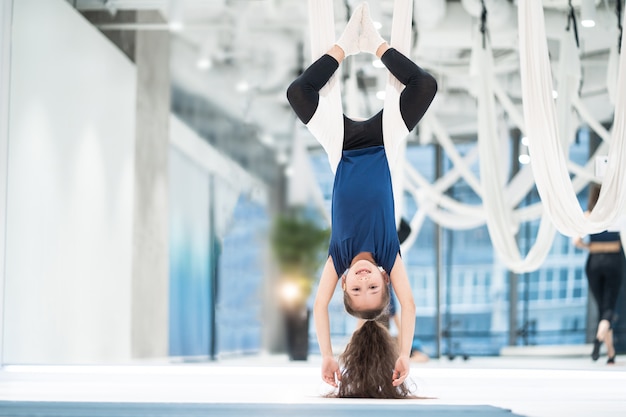 Free photo portrait of a beautiful young girl engaged in fly yoga on canvases.