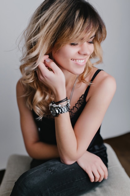 Portrait of a beautiful young girl, she sits on the chair in stylish black outfit, real emotion, smile.