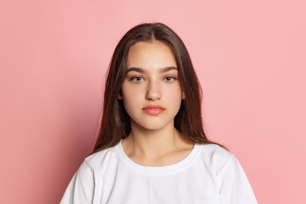 Portrait of beautiful young girl in white Tshirt posing looking at camera isolated over pink studio background