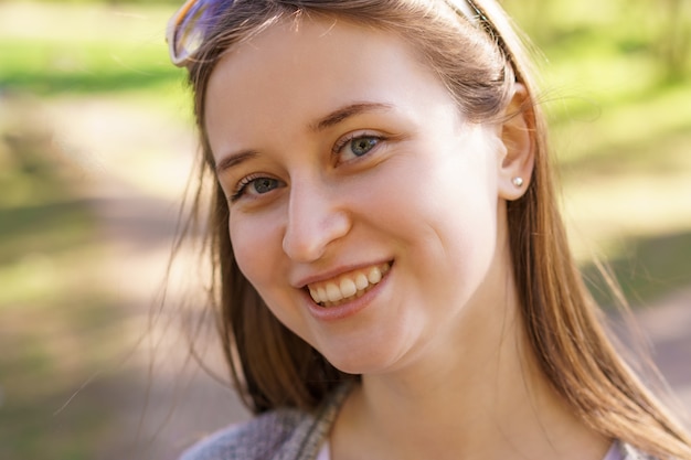 Портрет красивой молодой девушки с серьгой в ухе, которая улыбается в камеру в солнечный день