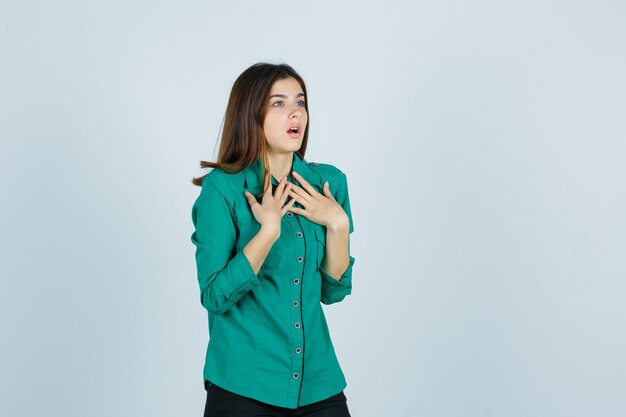 Portrait of beautiful young lady holding hands on chest in green shirt and looking shocked front view