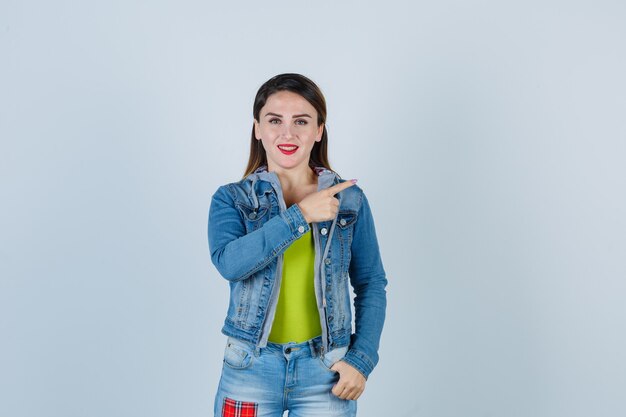 Portrait of beautiful young lady pointing right in denim outfit and looking cheerful front view