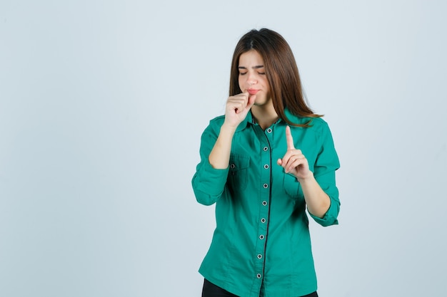 Portrait of beautiful young lady showing hold on a minute gesture while coughing in green shirt and looking sick front view