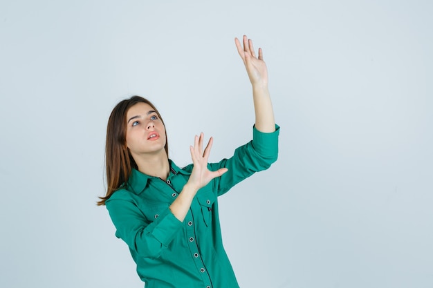 Portrait of beautiful young lady showing stop gesture in green shirt and looking frightened front view