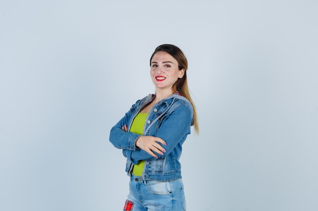 Portrait of beautiful young lady standing with crossed arms in denim outfit and looking cheery front view