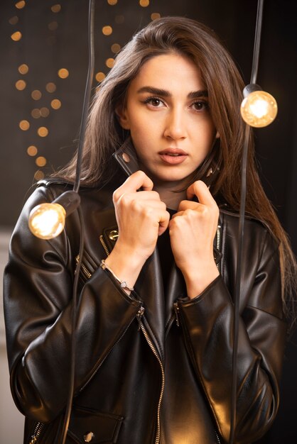 Portrait of a beautiful young model in black leather jacket posing near lamps.