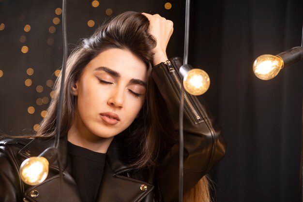 Portrait of a beautiful young model in black leather jacket posing near lamps.