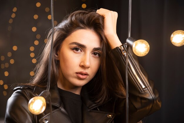 Portrait of a beautiful young model in black leather jacket posing near lamps.