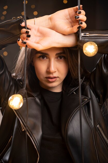 Portrait of a beautiful young model in black leather jacket posing near lamps.